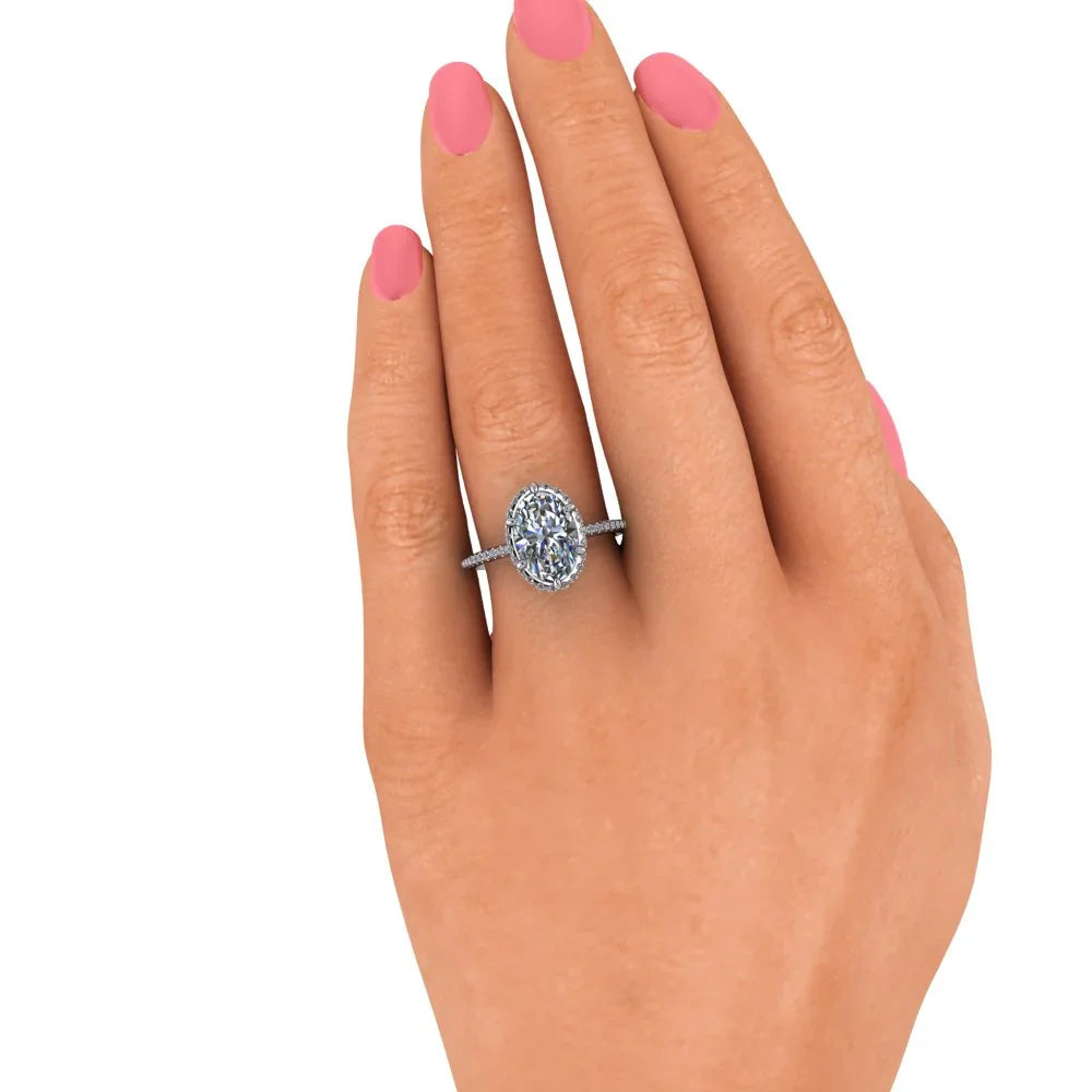 Hand with pink nails wearing a custom oval diamond engagement ring on a pavé band