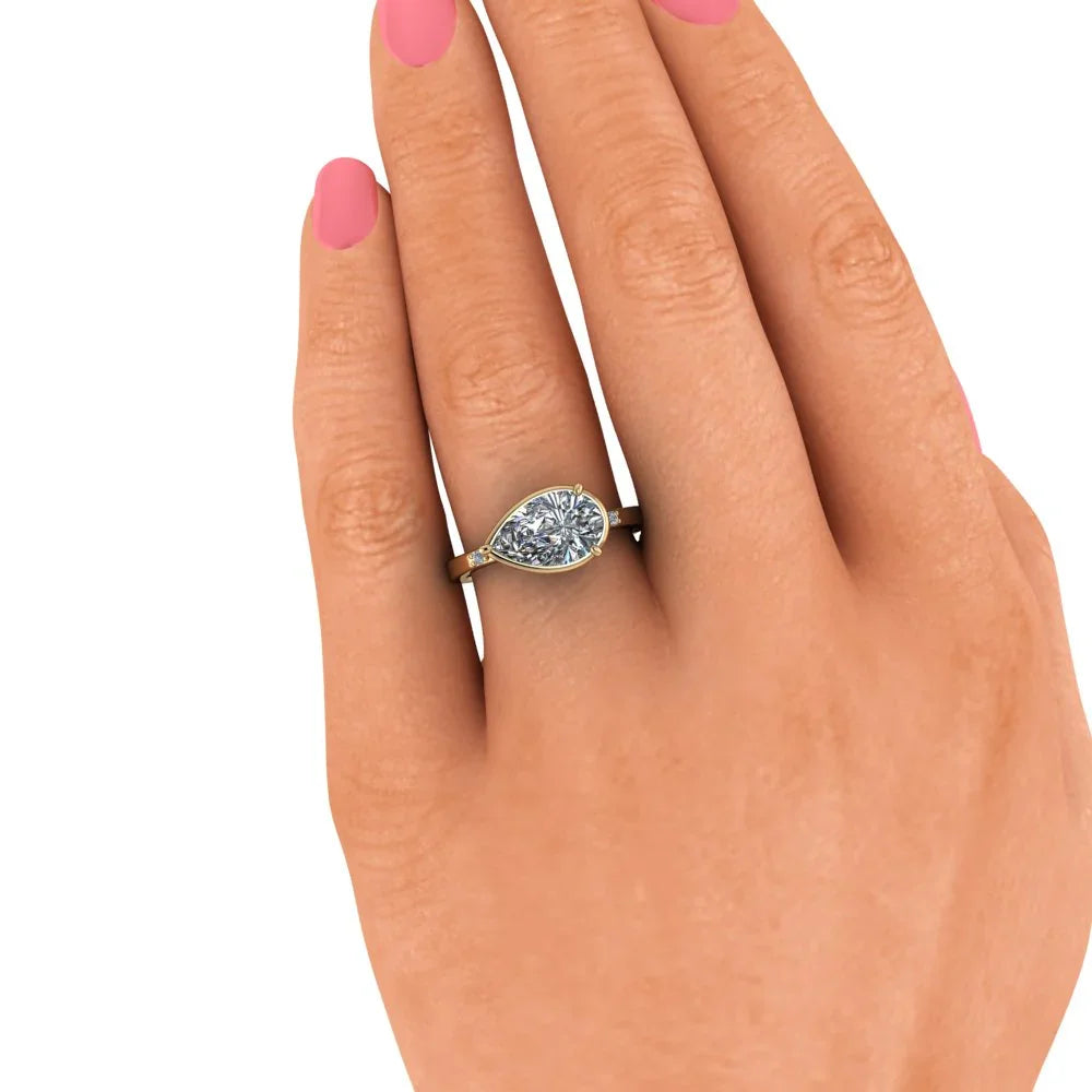 Hand wearing gold pear-shaped diamond engagement ring with pink manicured nails