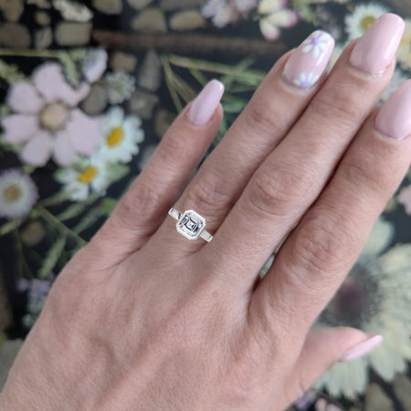 Hand wearing a geometric diamond engagement ring with floral nail art, floral background