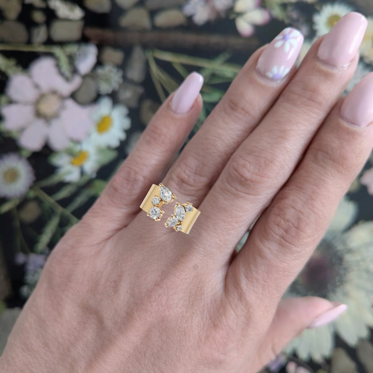 Gold open band ring with marquise and round diamonds on hand with floral nail art