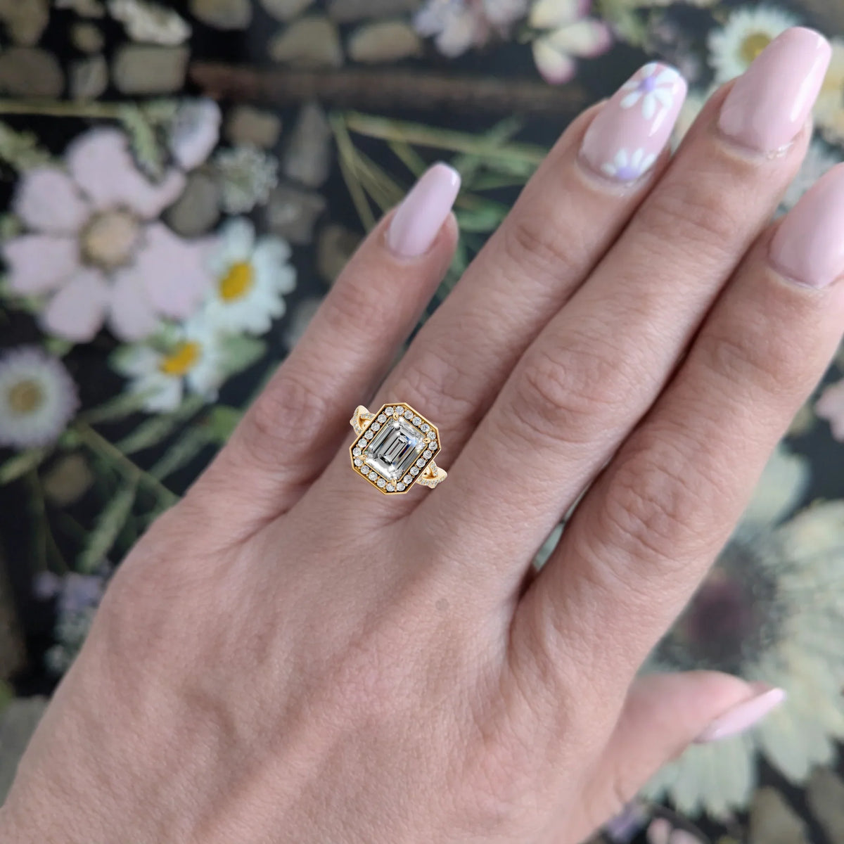 Gold diamond halo engagement ring on hand with floral background