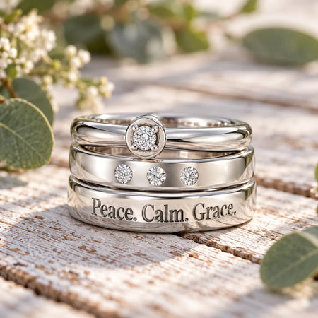 Three stacked silver custom rings with diamonds and 'Peace, Calm, Grace' engraving.