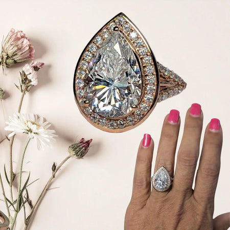 Pear-shaped diamond halo engagement ring on hand with pink nails, floral background
