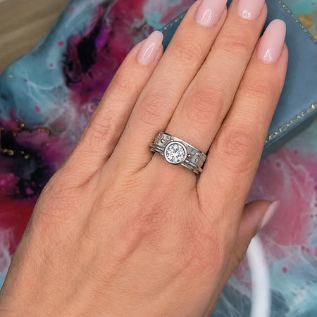 Custom engagement ring with round diamond and detailed band, worn on hand with soft pink nails