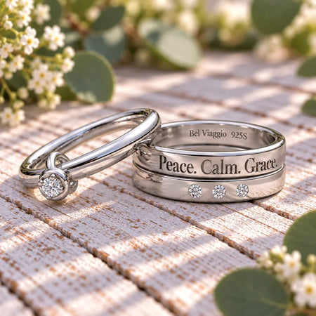 Two custom silver bands on a wooden surface, one with diamonds and 'Peace. Calm. Grace.' engraving.