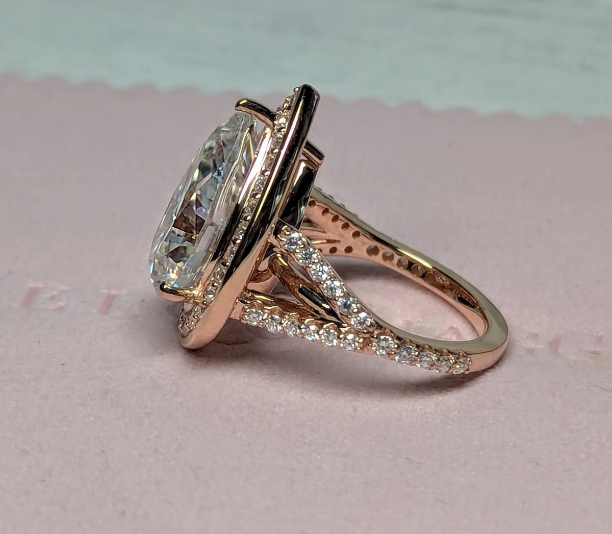 Rose gold custom engagement ring with oval center stone and pavé diamond band on blush background