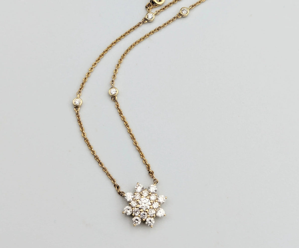 Gold chain necklace with diamond snowflake pendant and bezel-set diamonds on gray background