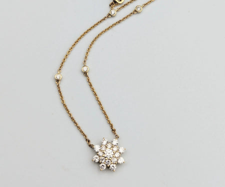Gold chain necklace with diamond snowflake pendant and bezel-set diamonds on gray background