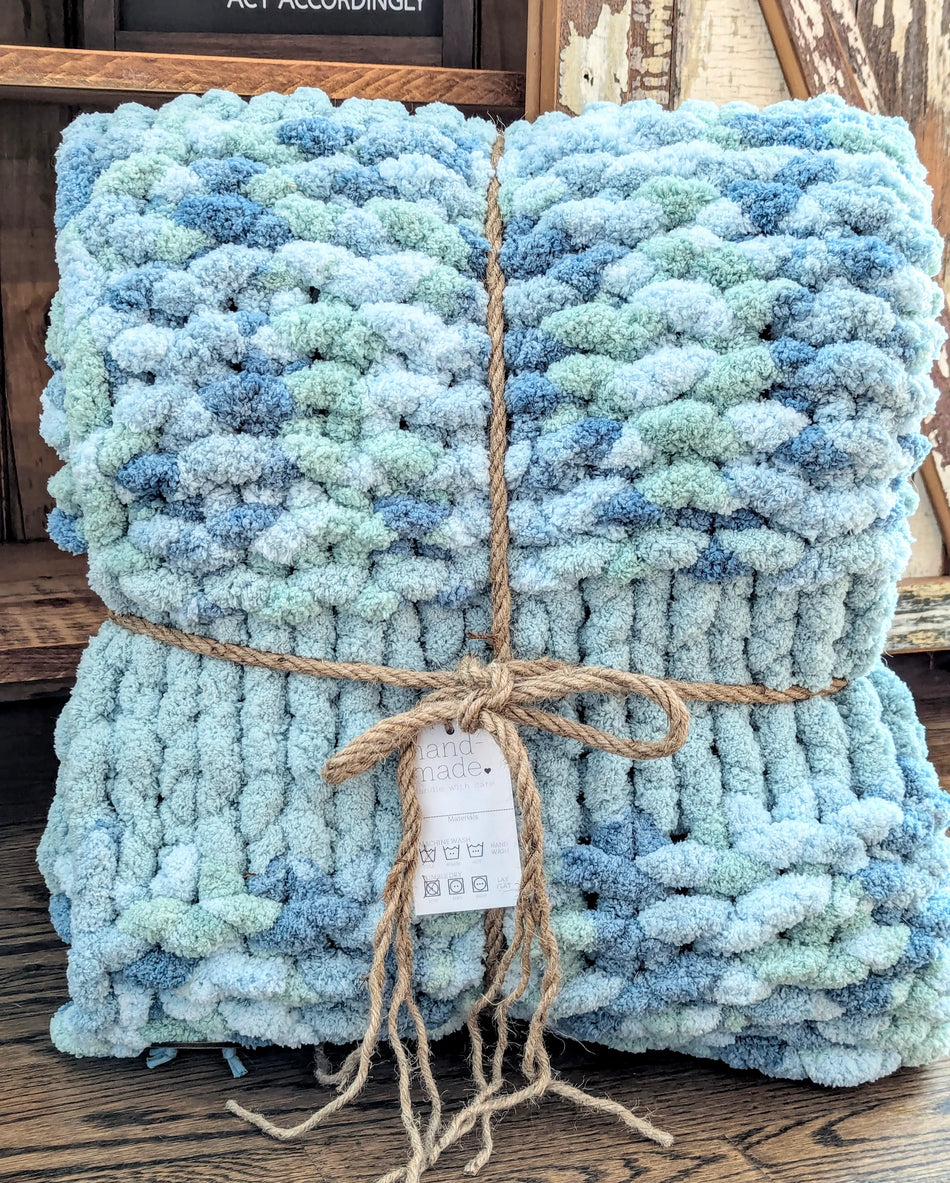 Handmade blue and green chunky knit blanket tied with twine on rustic wooden surface