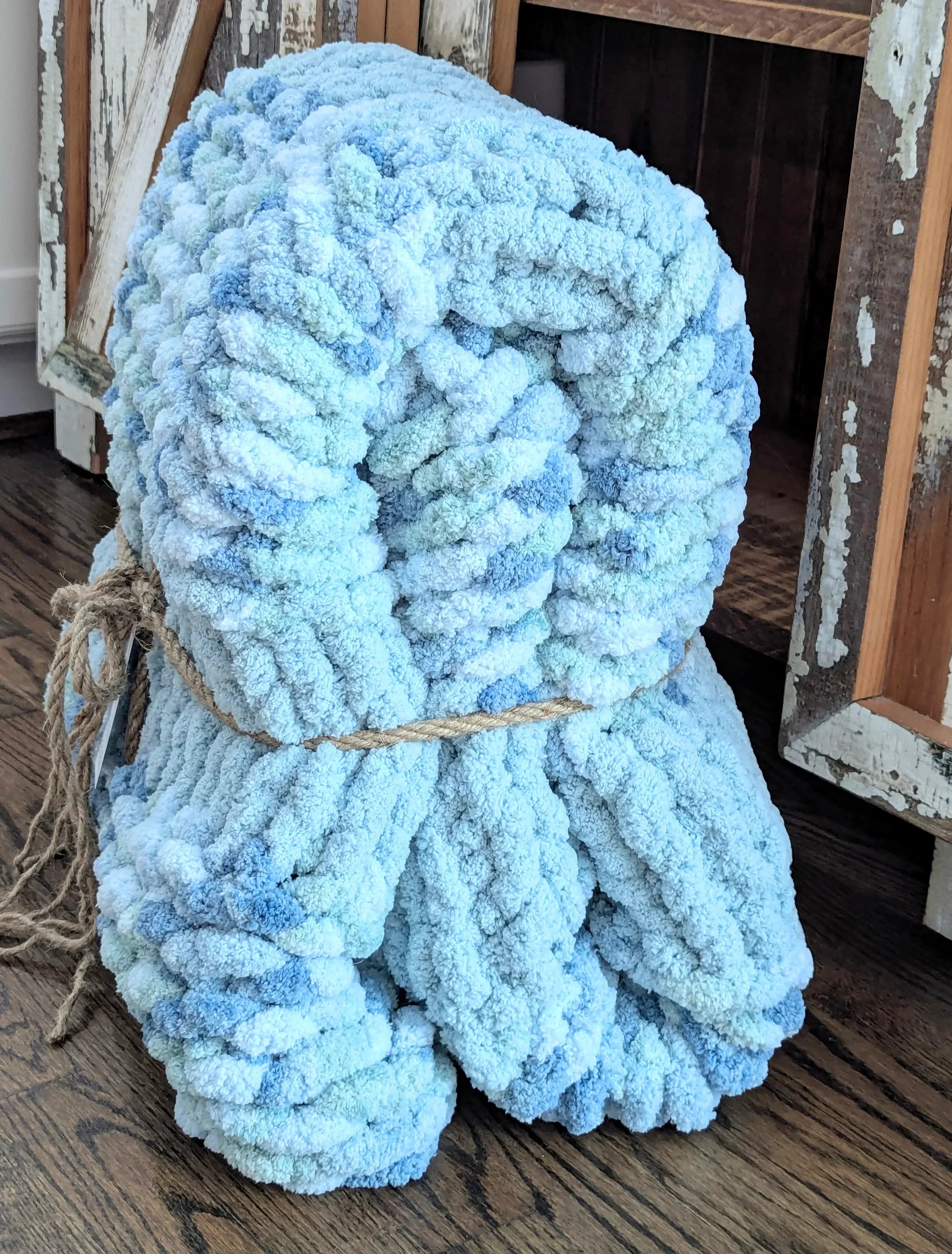 Chunky hand-knit blue and white blanket tied with twine on rustic wood floor