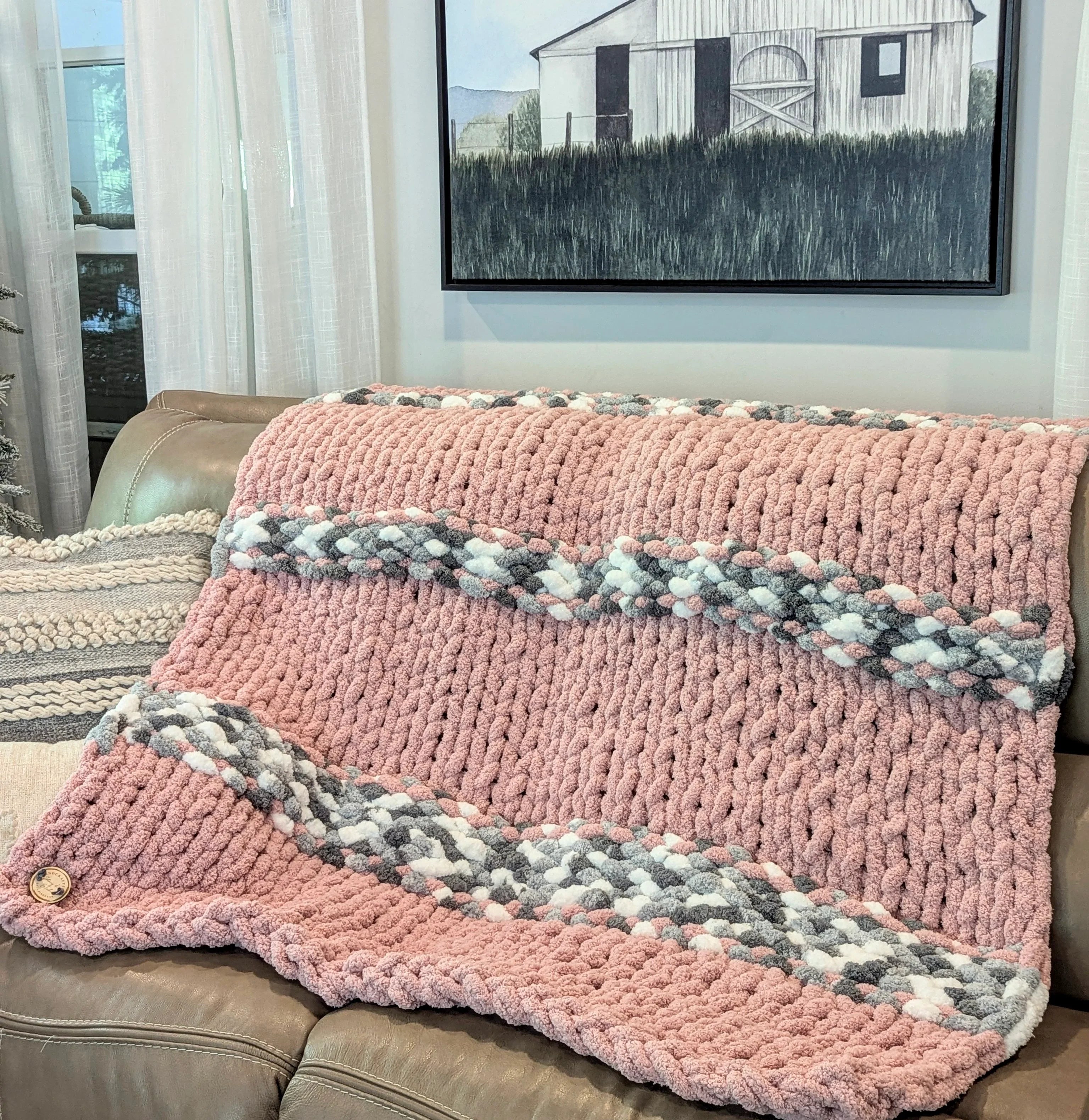 Chunky knit pink and gray throw blanket on a sofa in a cozy living room setting
