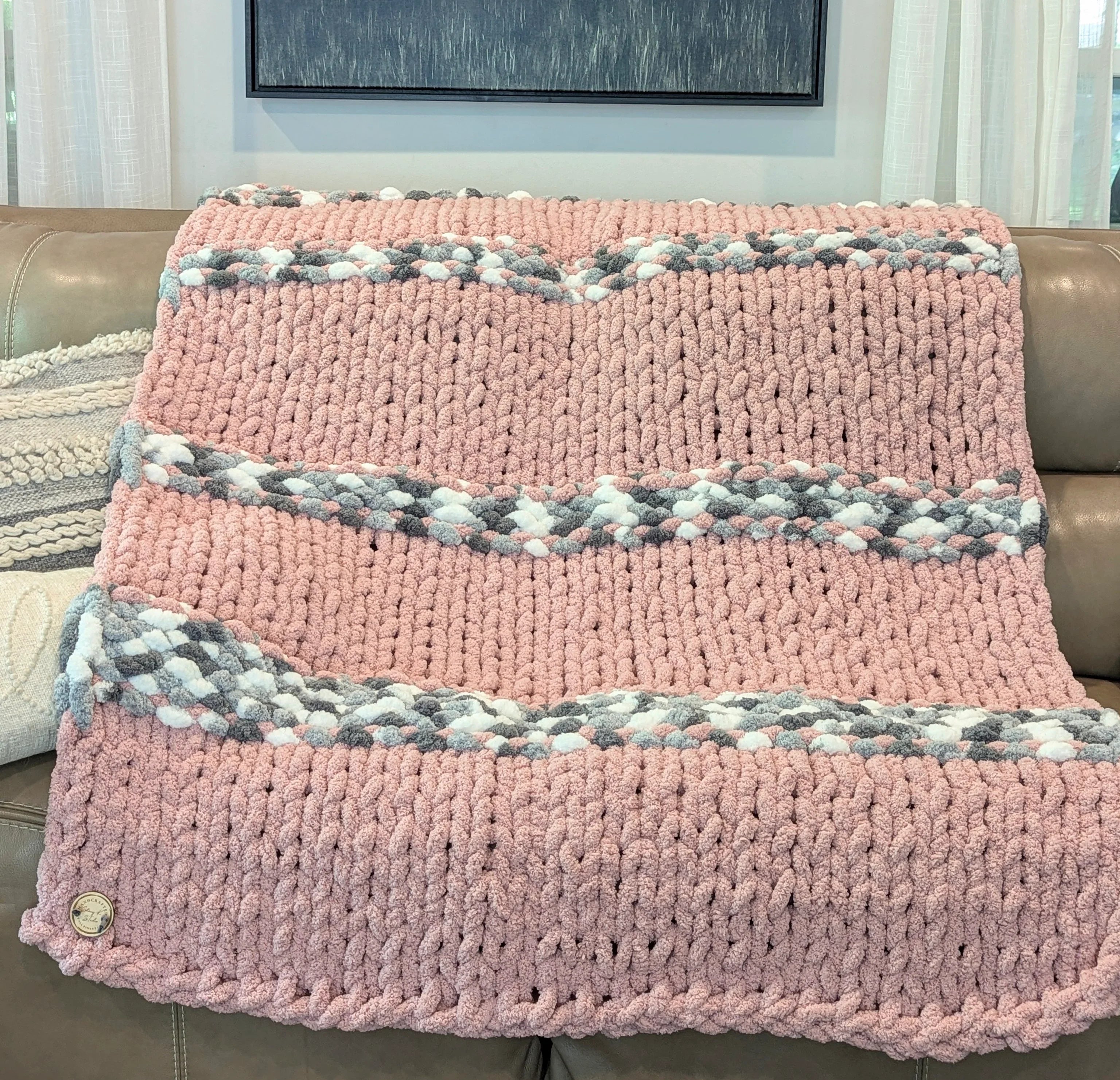 Chunky hand-knit pink blanket with grey and white stripes on a sofa