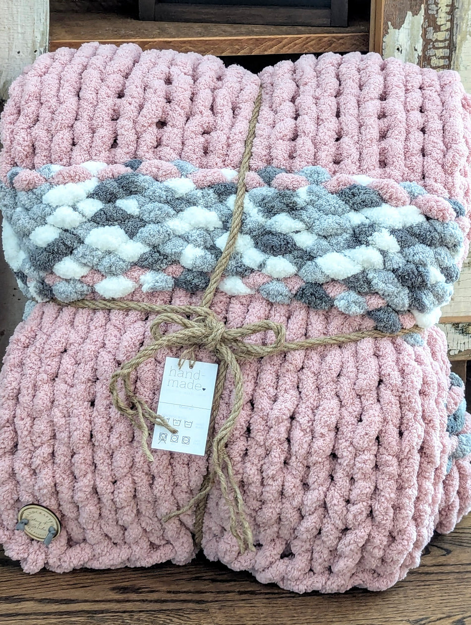 Chunky knit pink and gray handmade blanket with soft texture, tied with twine on wood surface