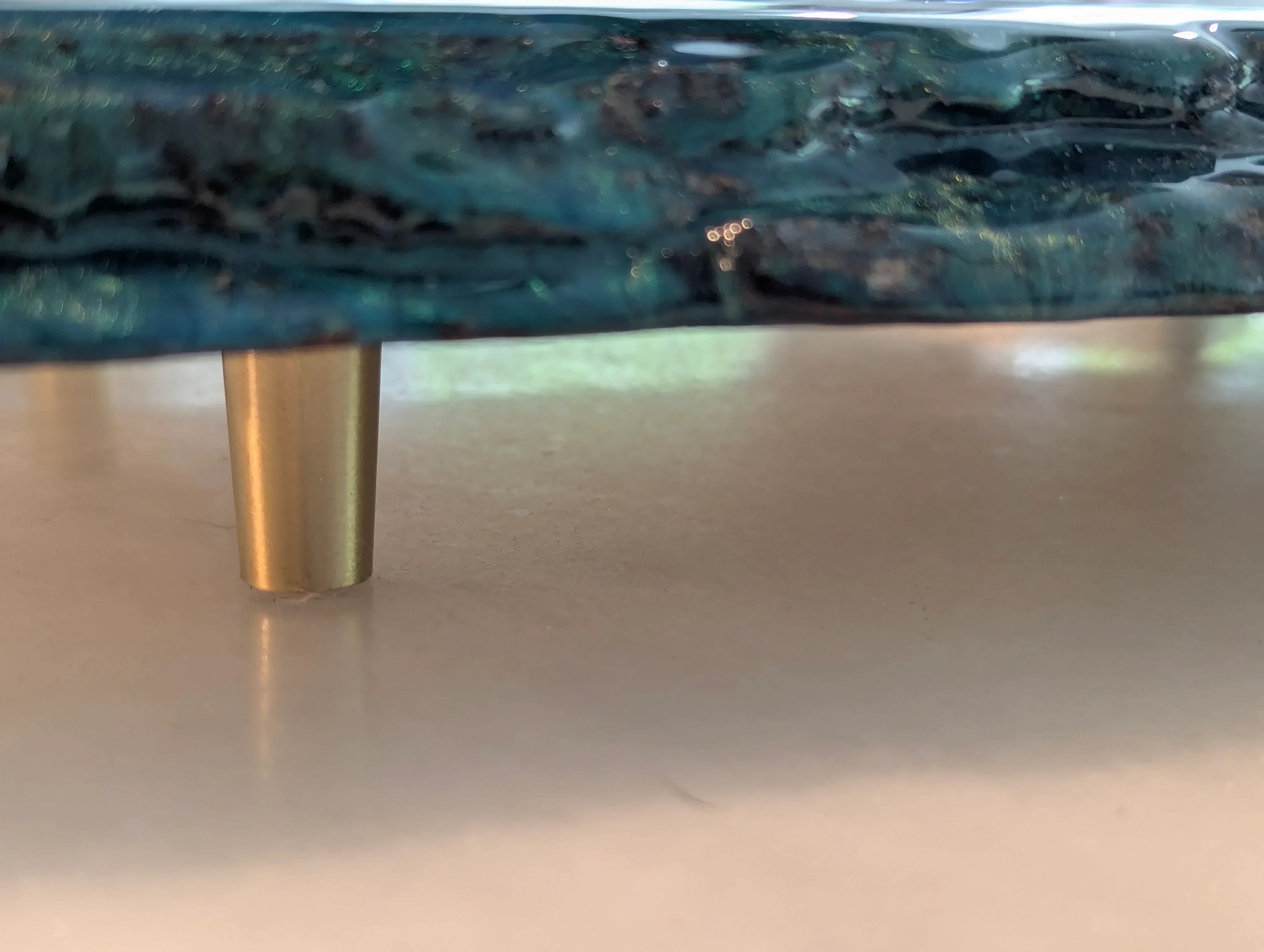 Close-up of a blue resin tray with gold metal leg on a light surface