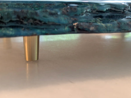 Close-up of a blue resin tray with gold metal leg on a light surface