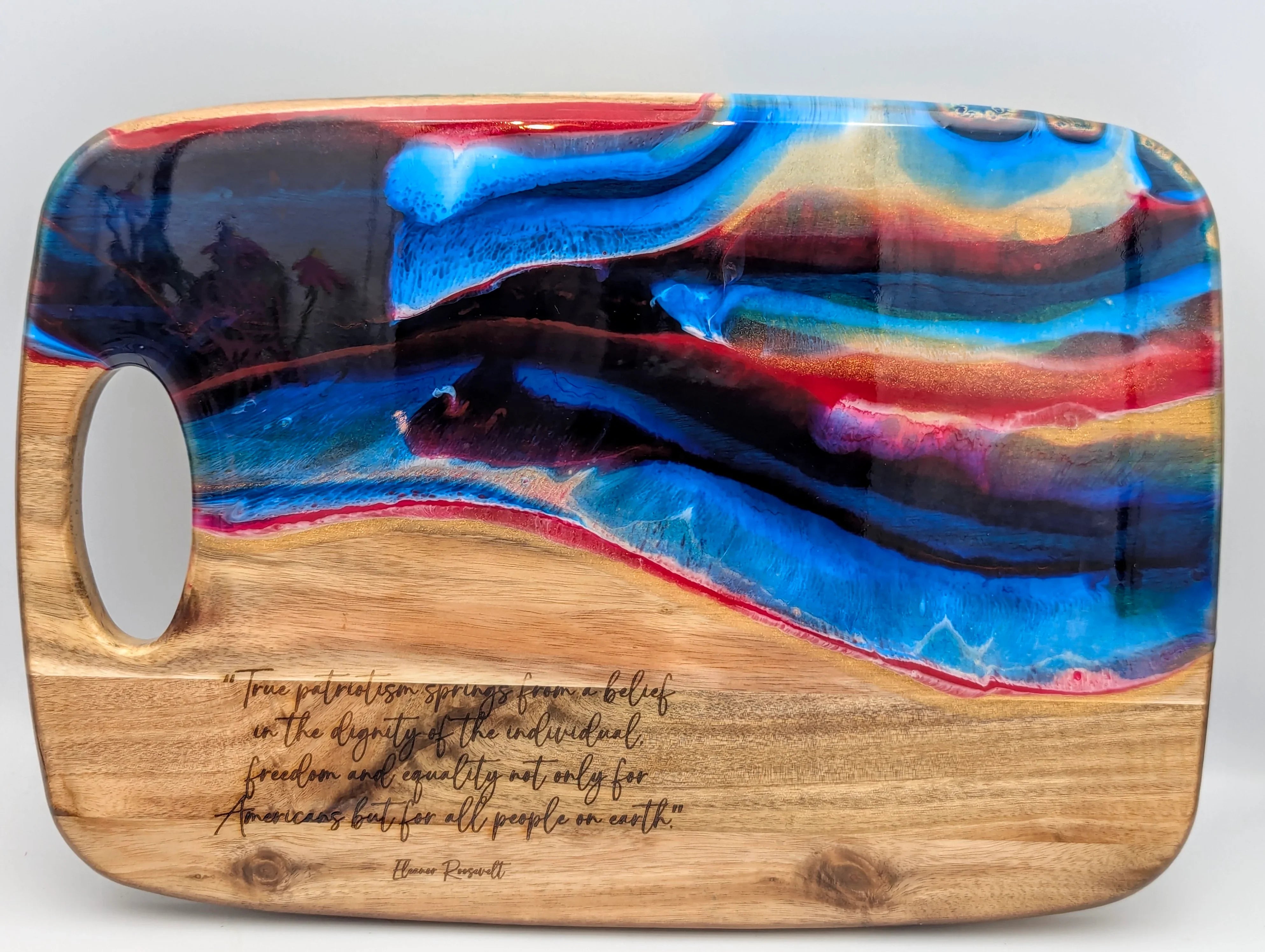 Wooden cutting board with abstract resin art in blue and red, engraved inspirational quote