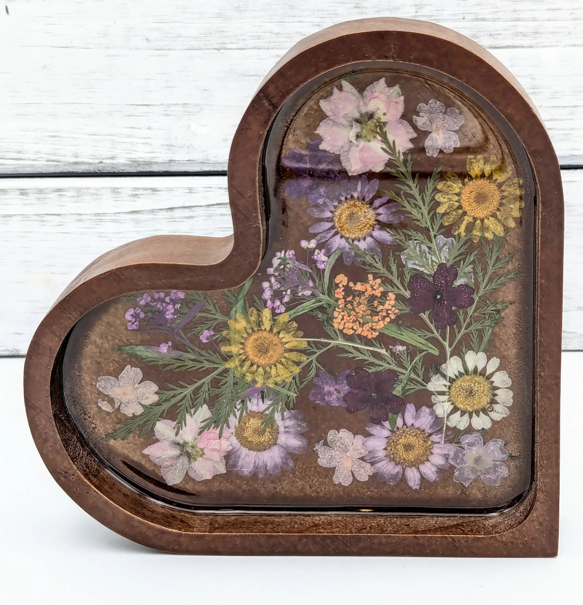 Heart-shaped wooden jewelry box with pressed flowers under resin, rustic background