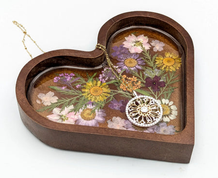 Gold floral pendant necklace on heart-shaped tray with pressed dried flowers