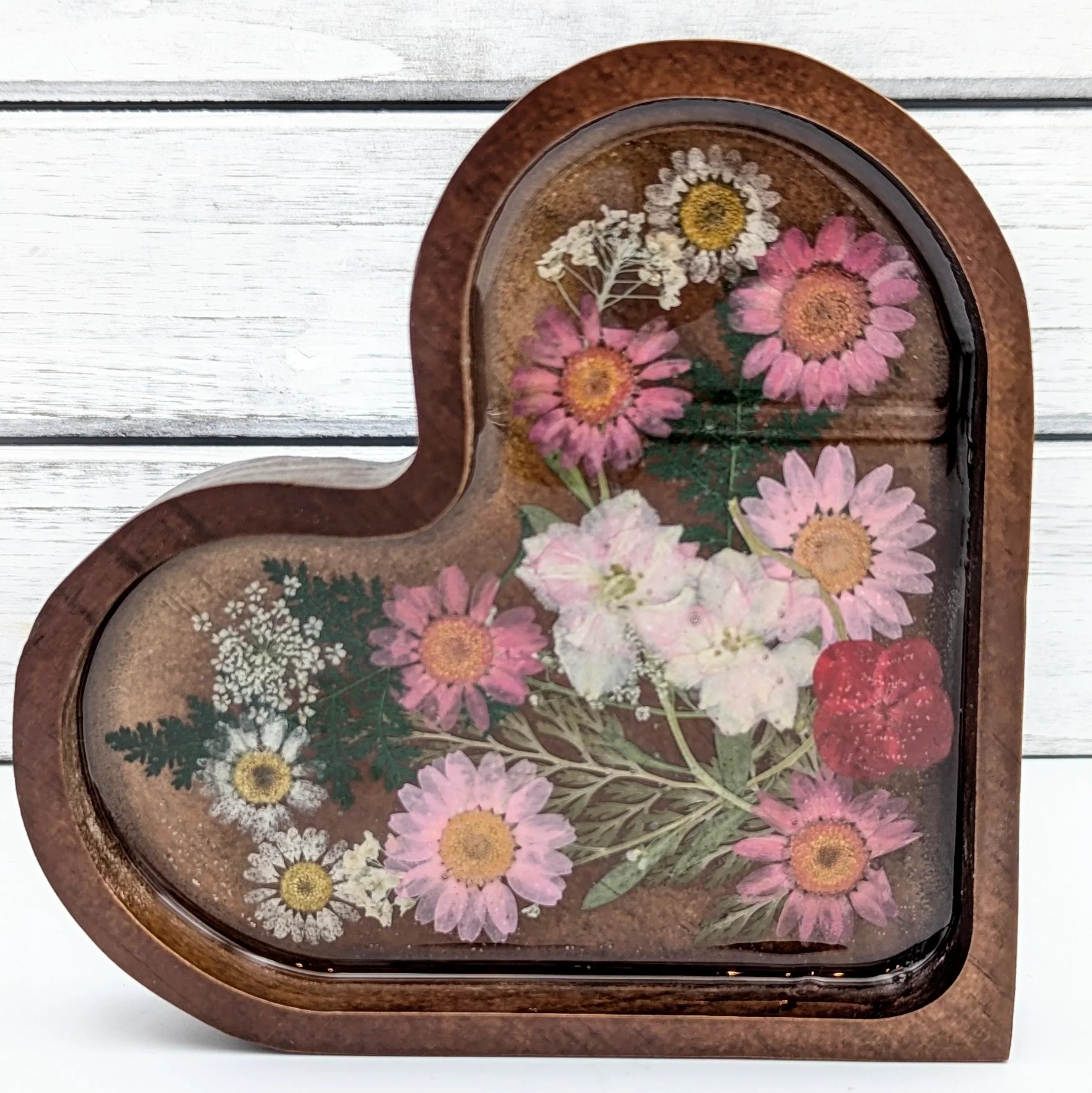 Heart-shaped resin tray with pressed pink daisies and white flowers on wood background