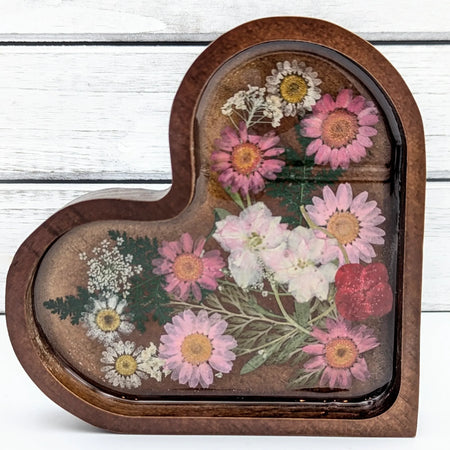 Heart-shaped resin tray with pressed pink daisies and white flowers on wood background