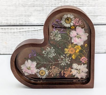 Heart-shaped resin keepsake with pressed flowers on wood background