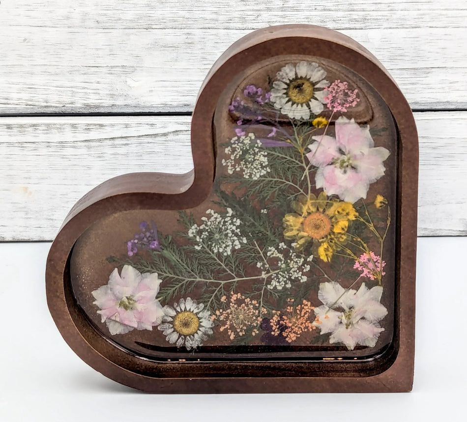 Heart-shaped resin keepsake with pressed flowers on wood background