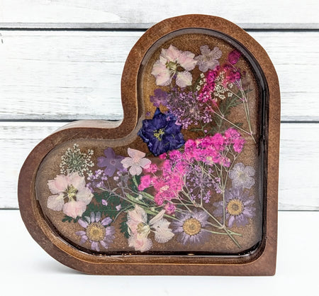Heart-shaped resin tray with pressed flowers in pink, purple, and white on wood background