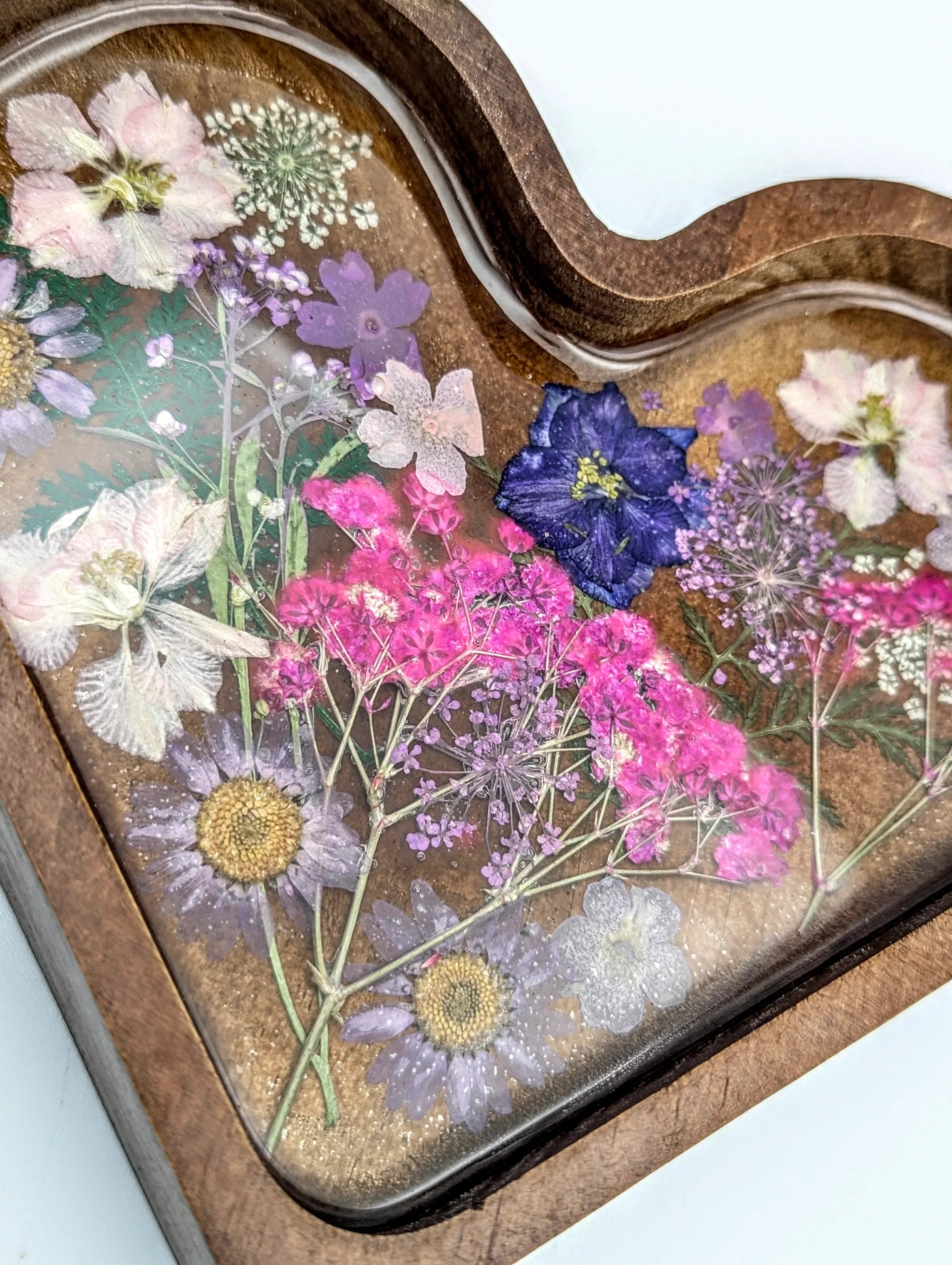 Heart-shaped wood tray with pressed colorful flowers under resin