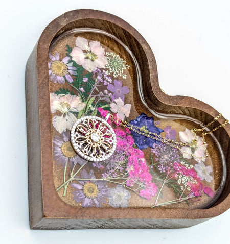 Gold and gemstone pendant necklace on a heart-shaped floral resin tray