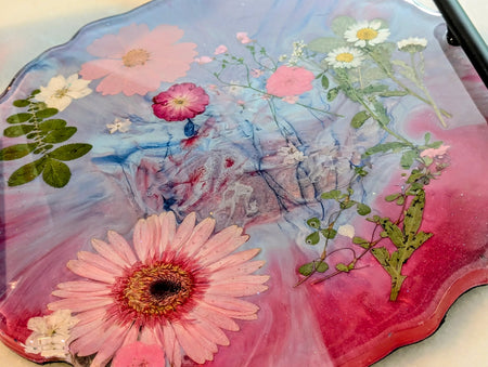 Epoxy resin art tray with pressed pink daisies, white chamomile, and green leaves in swirling blue-pink hues