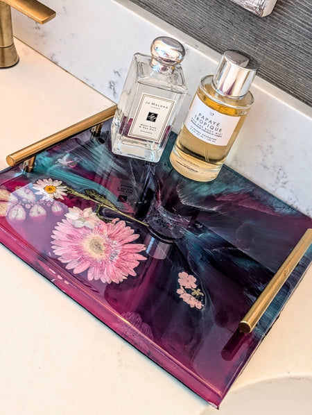 Epoxy resin tray with pressed flowers, holding Jo Malone and Le Monde Gourmand perfumes on marble countertop