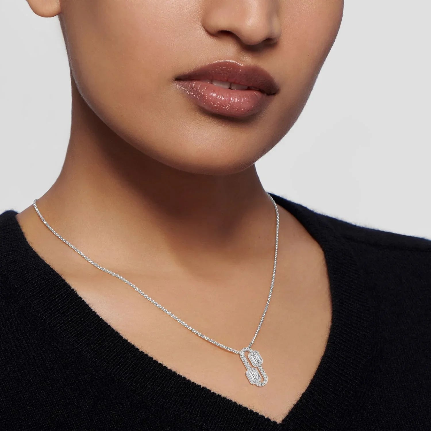 Elegant diamond pendant necklace with emerald-cut stones on a delicate chain, worn by woman in black top