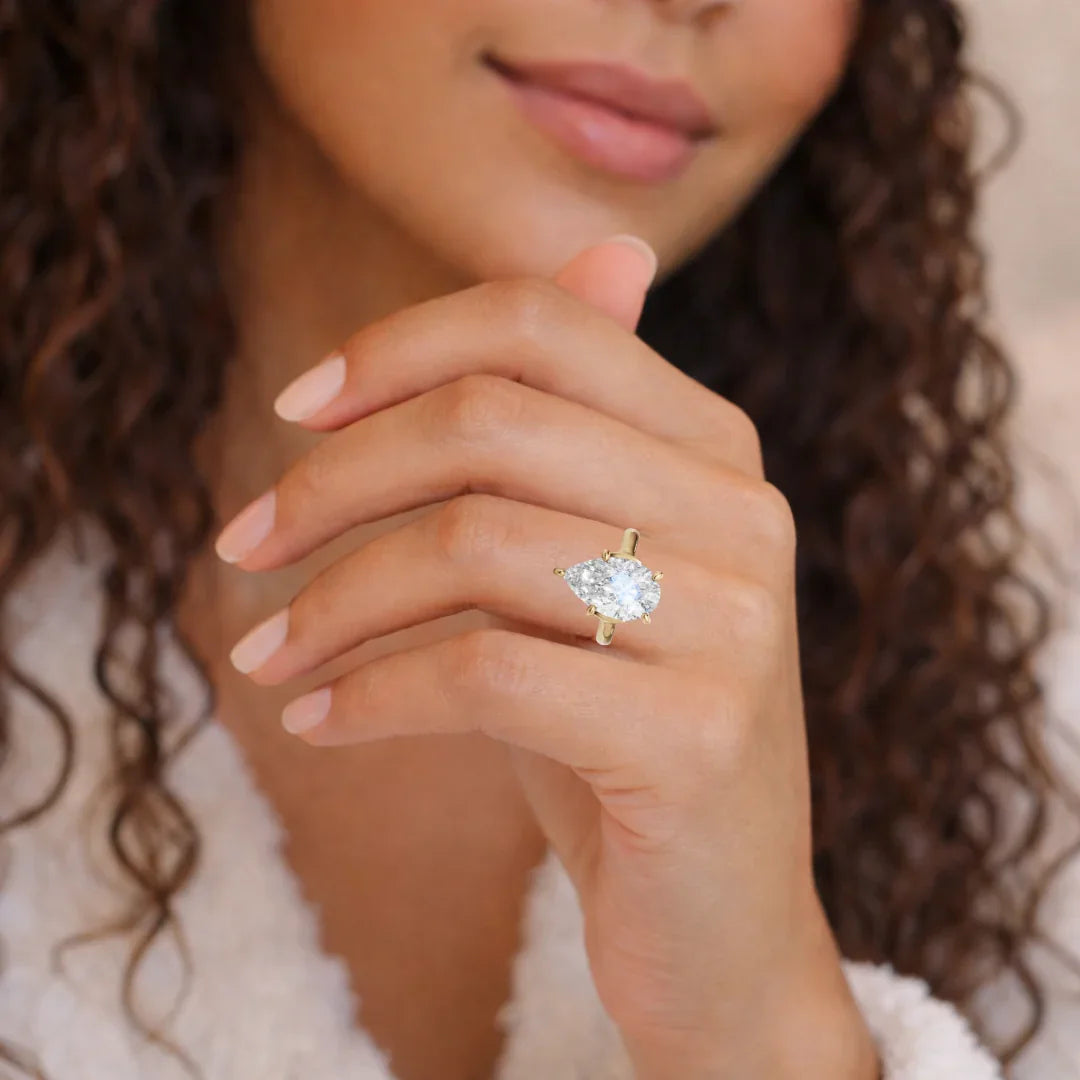 Woman wearing a gold band pear-shaped diamond engagement ring on hand