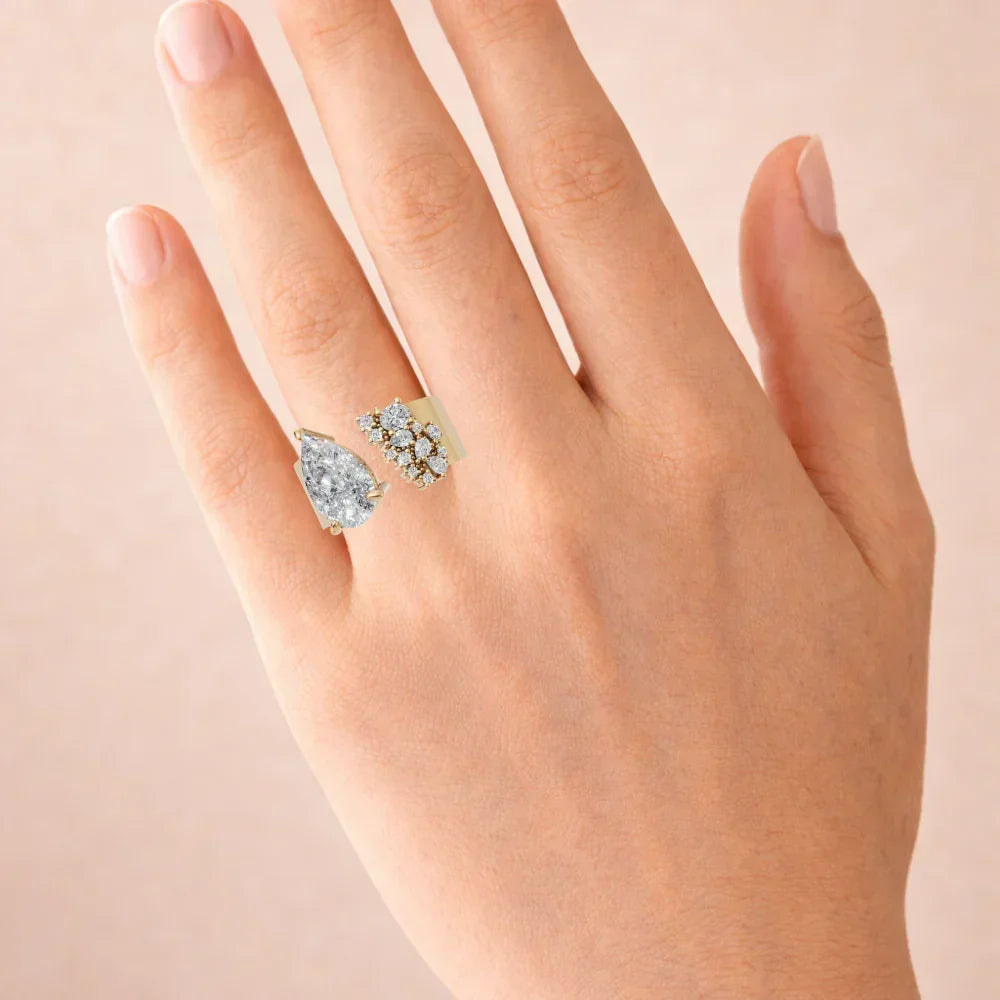 Hand wearing a unique open gold ring with a pear-shaped diamond and cluster accent