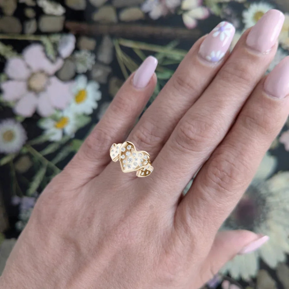 Hand wearing a gold heart-shaped ring with diamond accents