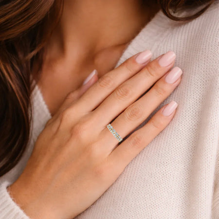 Woman wearing diamond eternity band ring on hand with light pink manicure