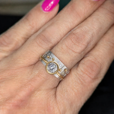 Custom engagement ring with round diamond, gold accent, and diamond band on hand