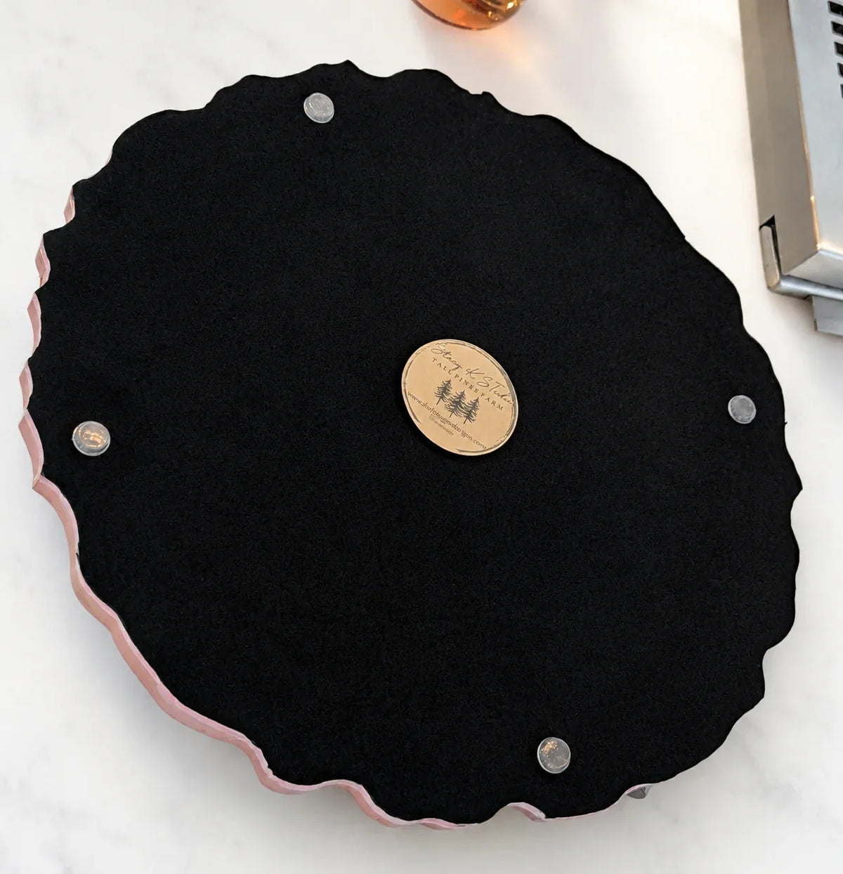 Black felt display tray with scalloped pink edge and brand emblem, ideal for showcasing custom jewelry.