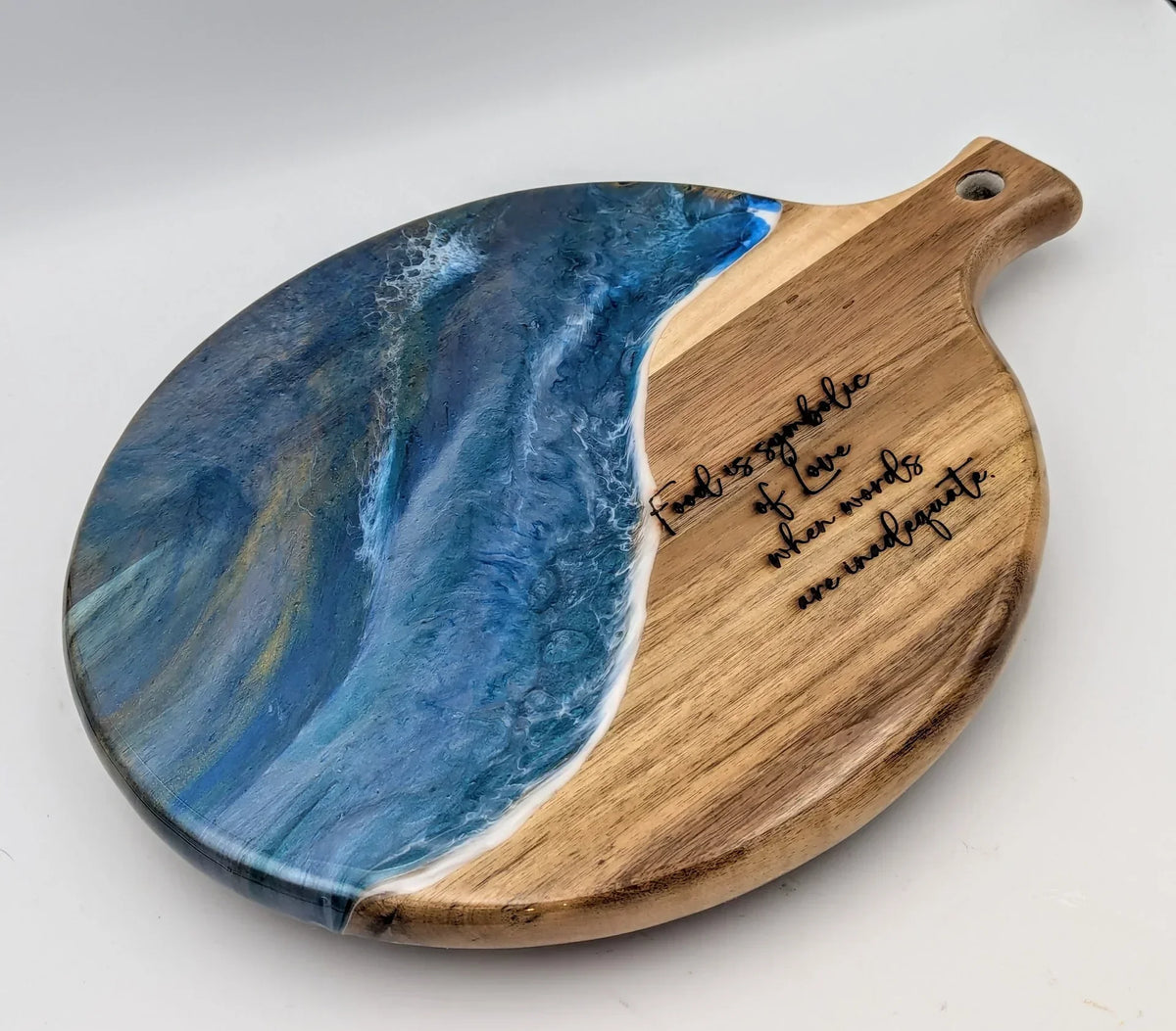 Round wooden serving board with blue resin ocean wave design and engraved love quote.