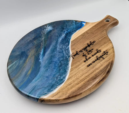 Round wooden serving board with blue resin ocean wave design and engraved love quote.