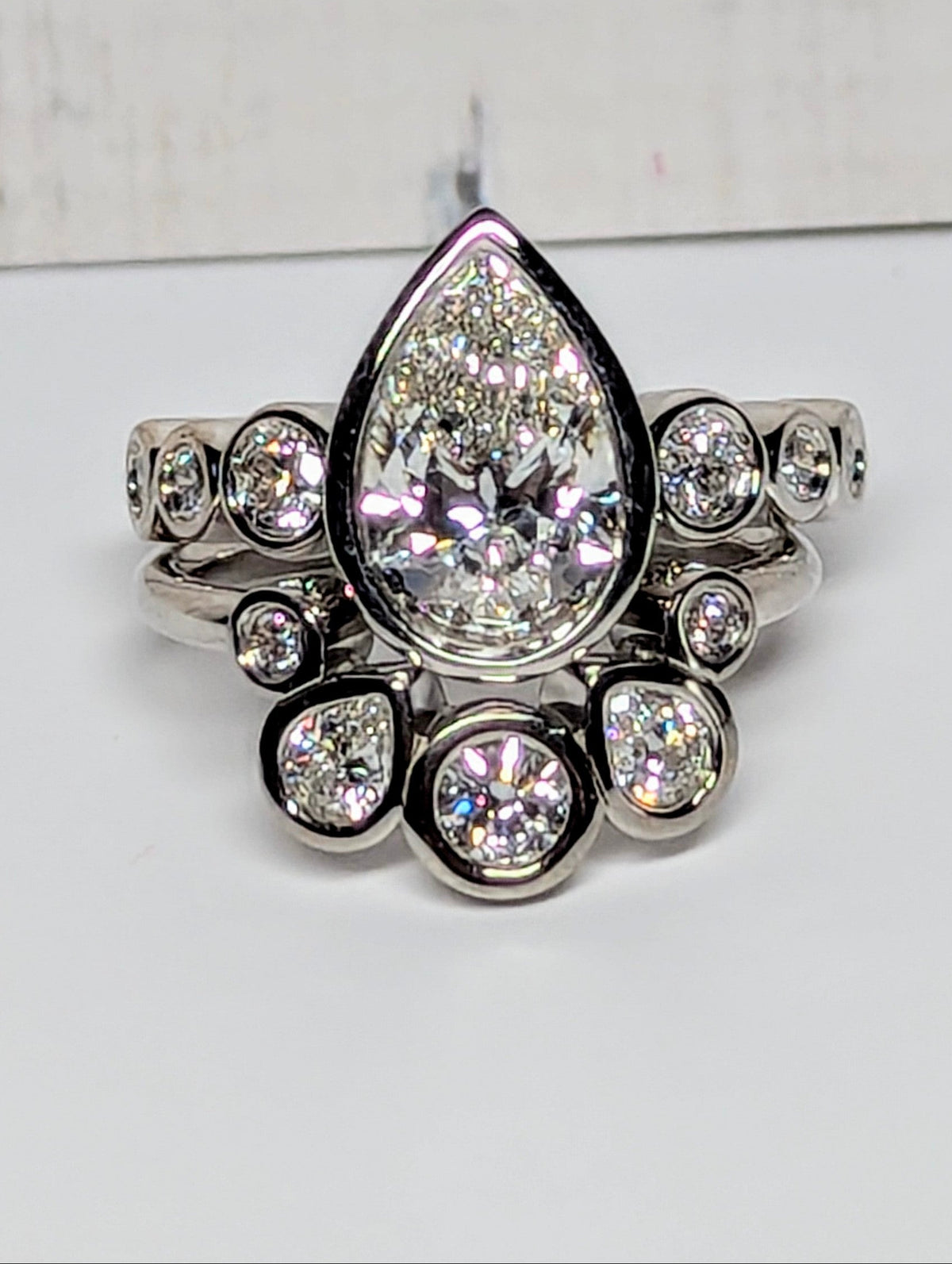 A silver-toned ring featuring a large teardrop-shaped clear center stone surrounded by smaller sparkling stones, set against a plain light background.