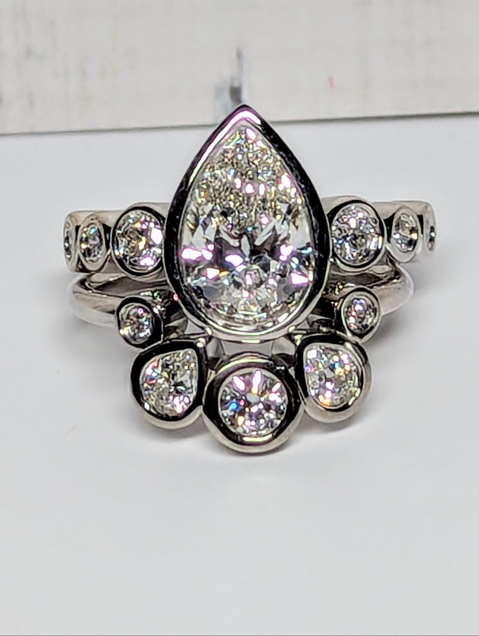 A silver-toned ring featuring a large teardrop-shaped clear center stone surrounded by smaller sparkling stones, set against a plain light background.