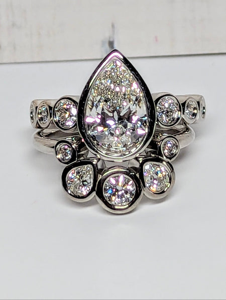 A silver-toned ring featuring a large teardrop-shaped clear center stone surrounded by smaller sparkling stones, set against a plain light background.