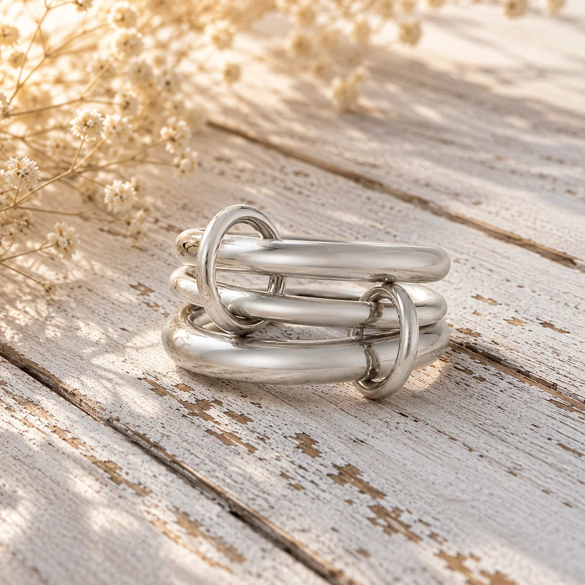 Modern silver link ring stack on rustic wood with dried flowers, custom jewelry design