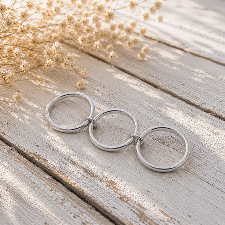 Three interlocking silver rings on rustic wood with dried flowers, custom engagement ring design