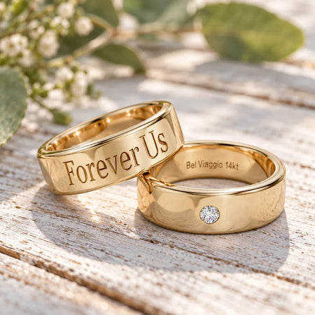 Two gold wedding bands on weathered wood, one engraved 'Forever Us' and one with a diamond.