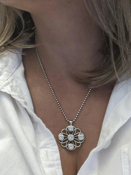 Woman wearing a silver flower-shaped pendant necklace with round clear gemstones.