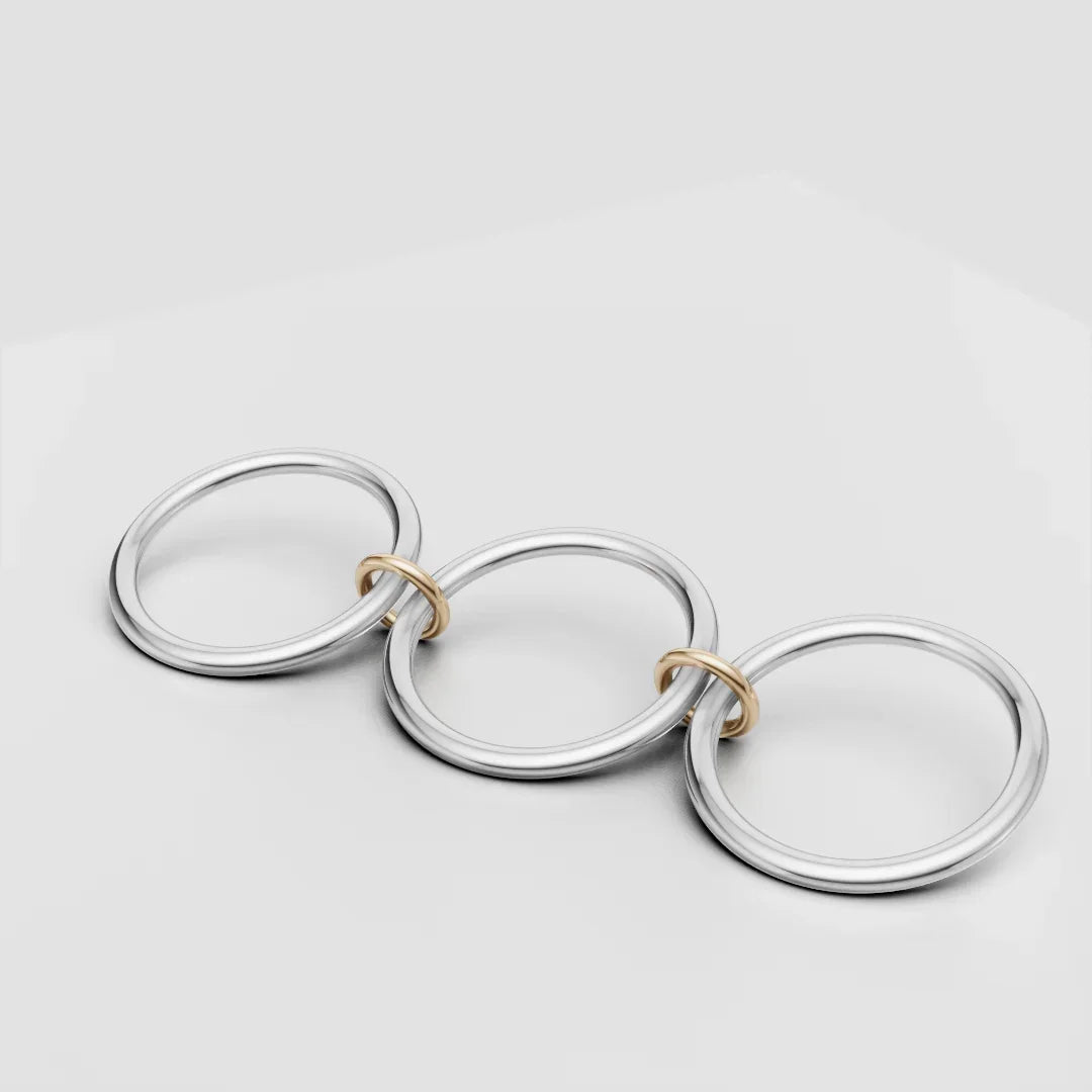 Three large silver rings linked by small gold rings on a white background, modern jewelry design