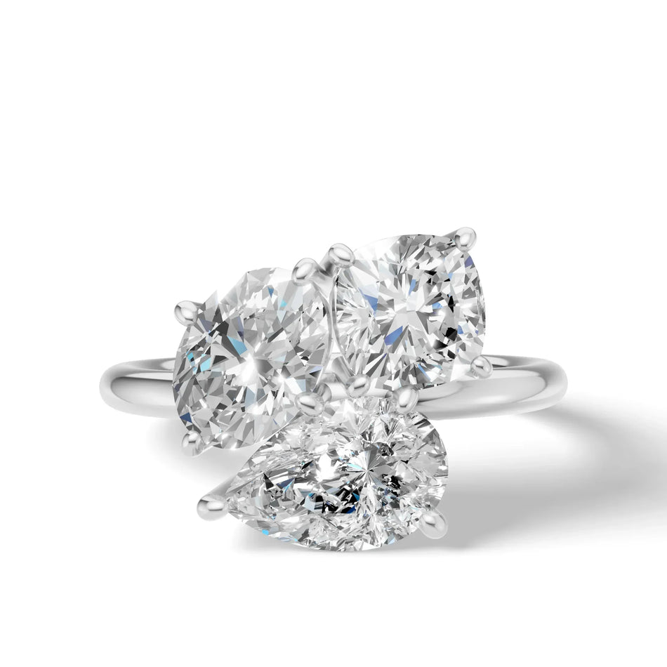 Platinum ring with three large diamonds in pear and cushion cuts on a white background