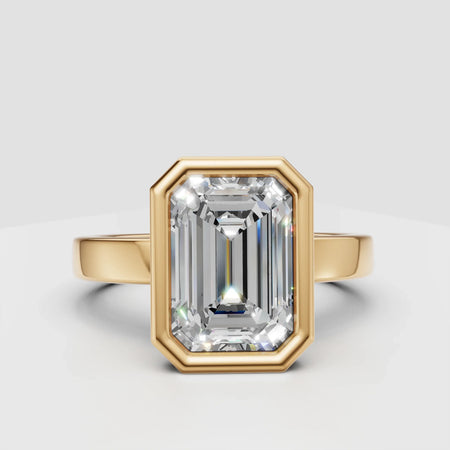 Emerald cut diamond engagement ring with yellow gold setting on white background